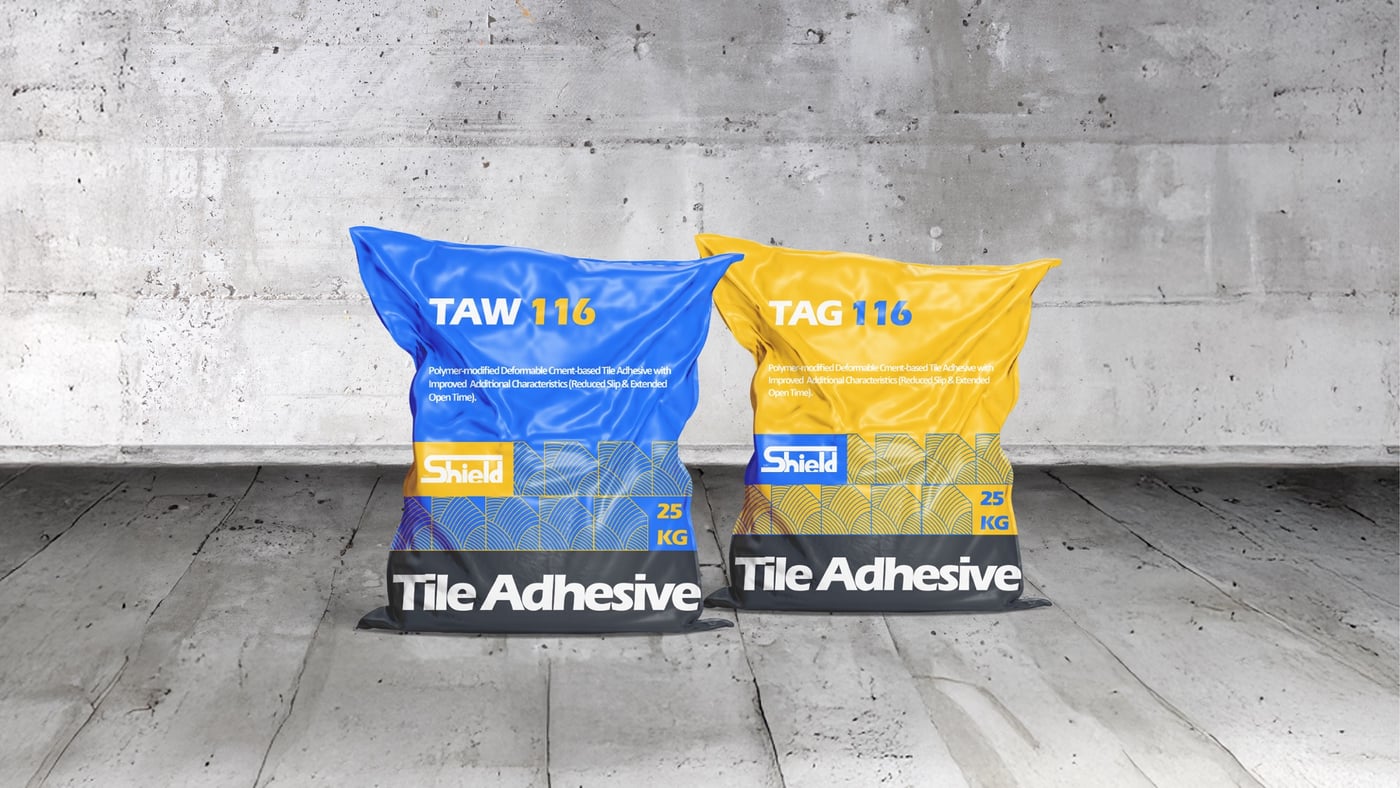 Two Shield tile adhesive bags in blue and yellow variants on wood floor